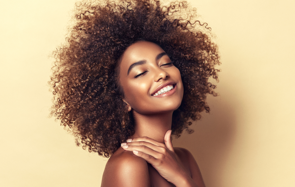 Beauty,Portrait,Of,African,American,Woman,With,Clean,Healthy,Skin A woman with natural hair closes her eyes and smiles, showing her dental implants.